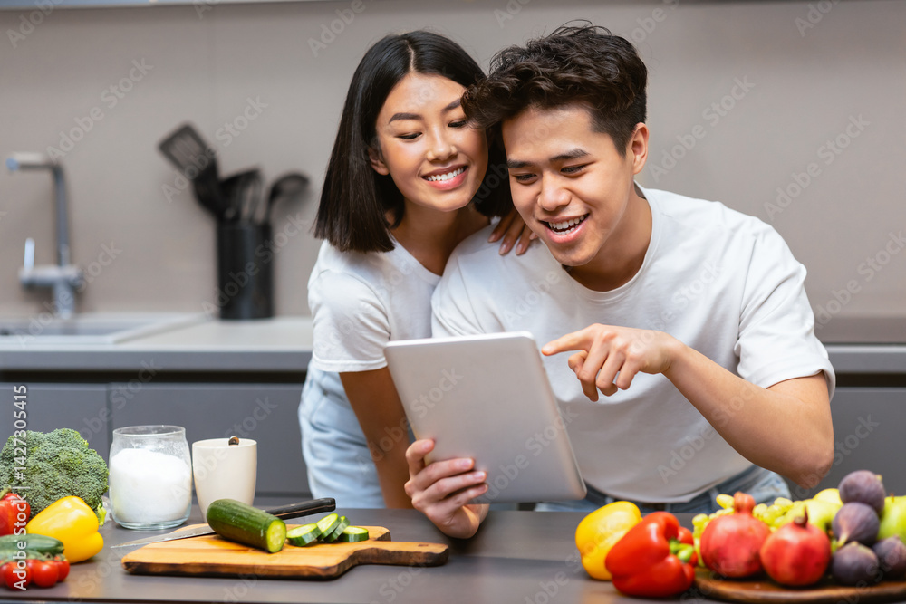 Korean Husband And Wife Cooking Using Digital Tablet Preparing Dinner Together In Modern Kitchen At Home. Food Recipes Online, Cooking Application Concept Korean Husband And Wife Cooking Using Digital Tablet Preparing Dinner Together In Modern Kitchen At Home. Food Recipes Online, Cooking Application Concept