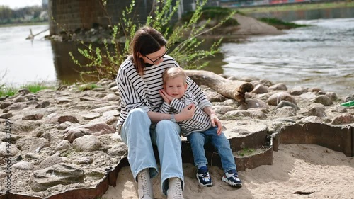 Mother and son hug and smile on the sunny Vistula riverbank in Warsaw, sharing a warm summer moment by the water.
