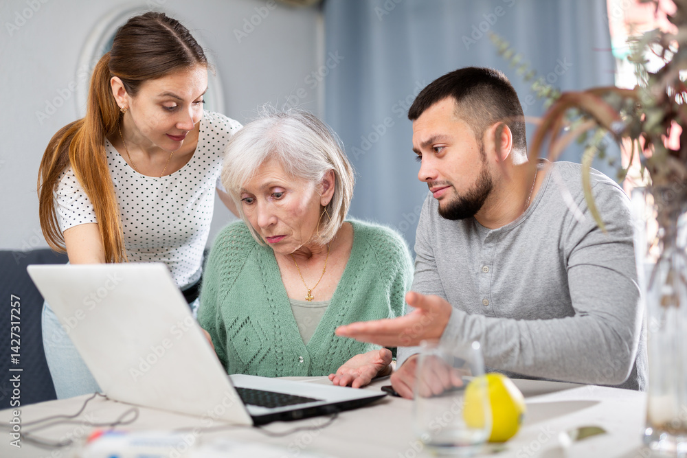 Young adult son and his wife giving help with laptop to stressed elderly mother at home Young adult son and his wife giving help with laptop to stressed elderly mother at home