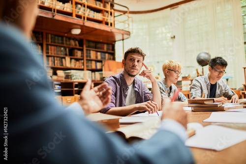 Young and diverse group of students studying in a university library with the help of their professor