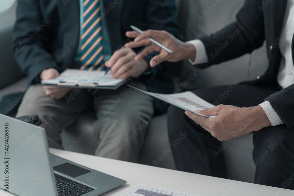 Business people having serious conversation on sofa in living room while another person is listening with laptop. Close up.