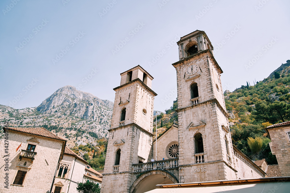 Fototapeta premium Bell towers of the Cathedral of St. Tryphon among ancient houses at the foot of the mountains. Kotor, Montenegro