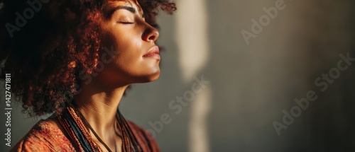 Obraz na płótnie A woman with curly hair closes her eyes, basking in soft light, evoking a serene and peaceful moment. w salonie