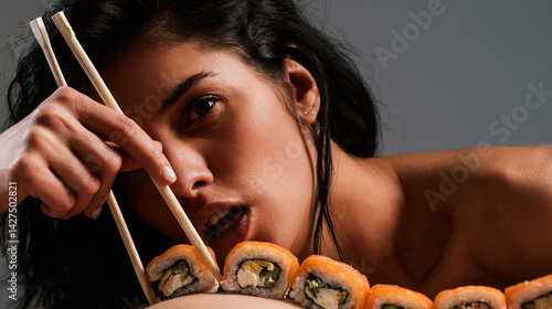 Obraz na płótnie Sushi closeup in sexy woman mouth. Sexy woman eating sushi with chopsticks. Model eat sashimi. Sensual bite of sushi. Female tasting nigiri. Lunch at Japanese restaurant. Desire for delicious sushi. w salonie