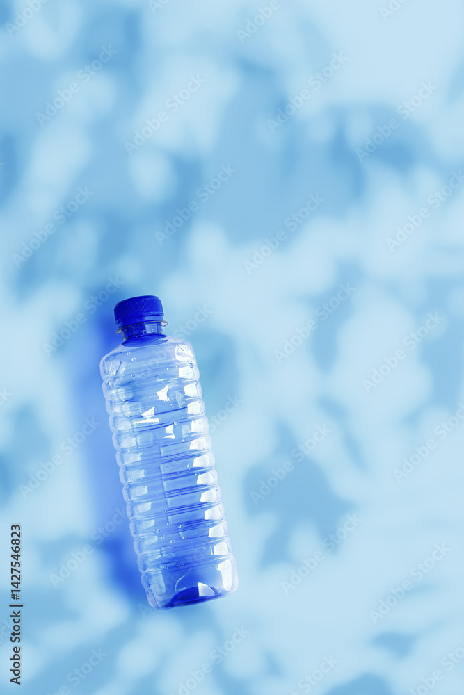 Transparent plastic water bottle on blue surface, shadows from leaves, aesthetic top view vertical photo, copyspace, Eco trend to reduce disposable plastics, Pollution, environmental protection