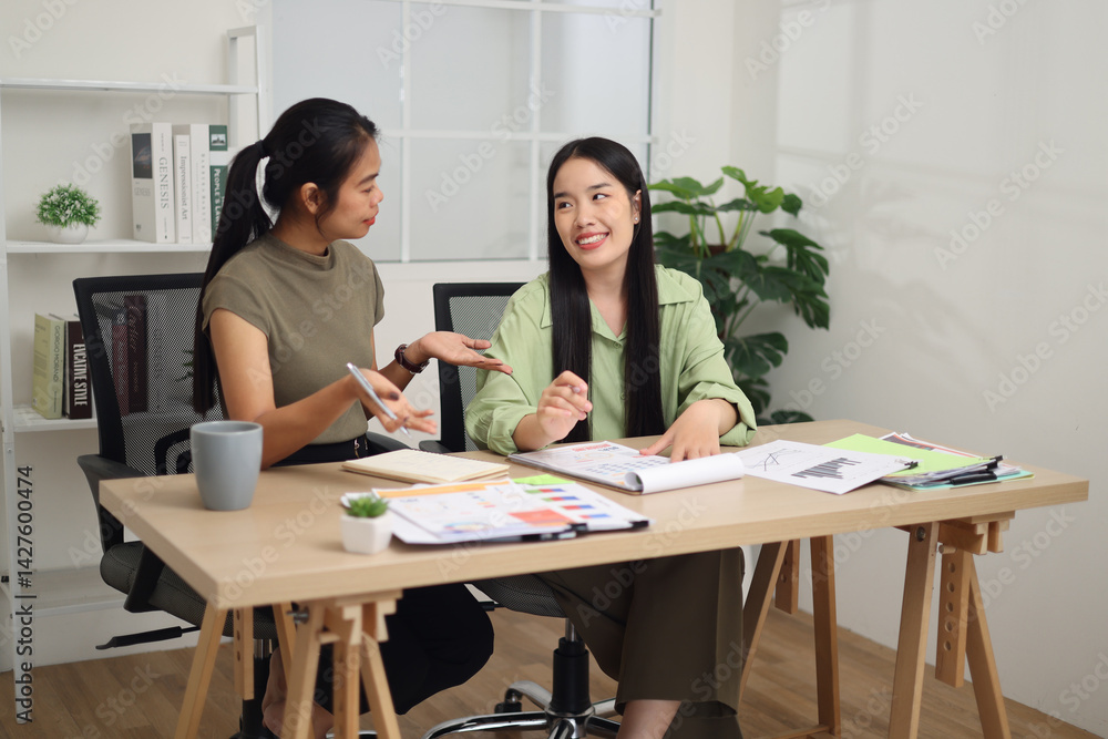 Portrait of Two female colleagues are sitting together at desk, reviewing documents and discussing work in the office.