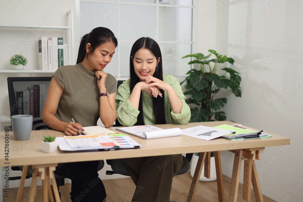 Portrait of Two female colleagues are sitting together at desk, reviewing documents and discussing work in the office.