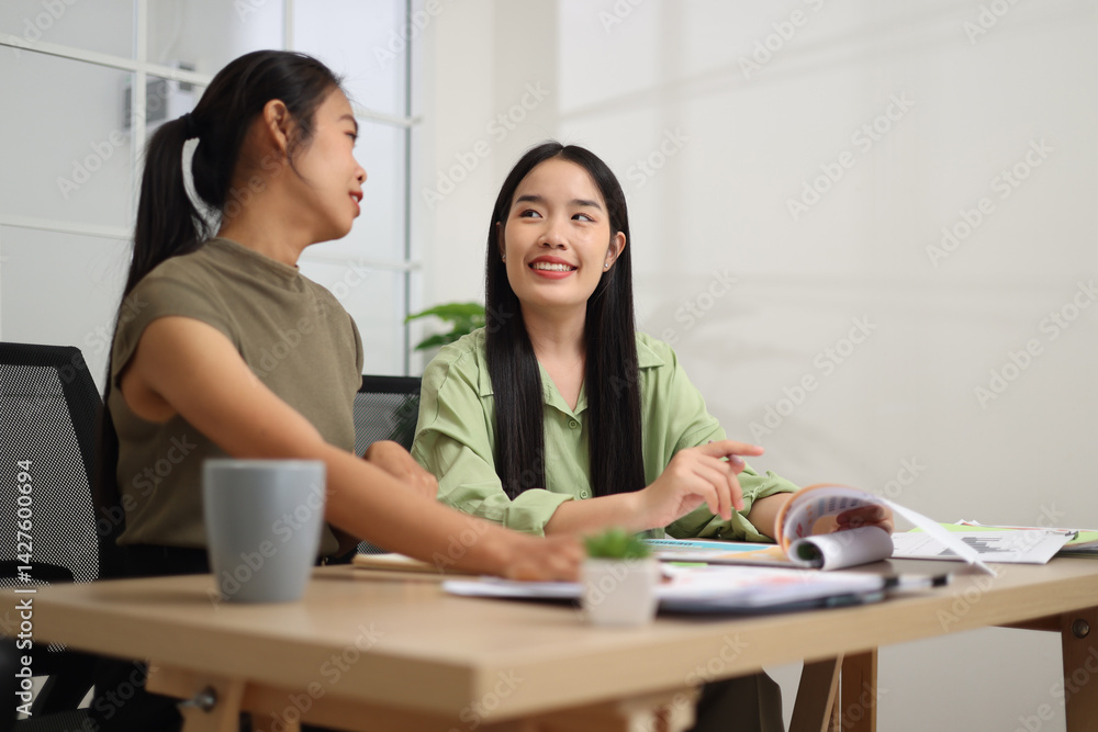 Portrait of Two female colleagues are sitting together at desk, reviewing documents and discussing work in the office.
