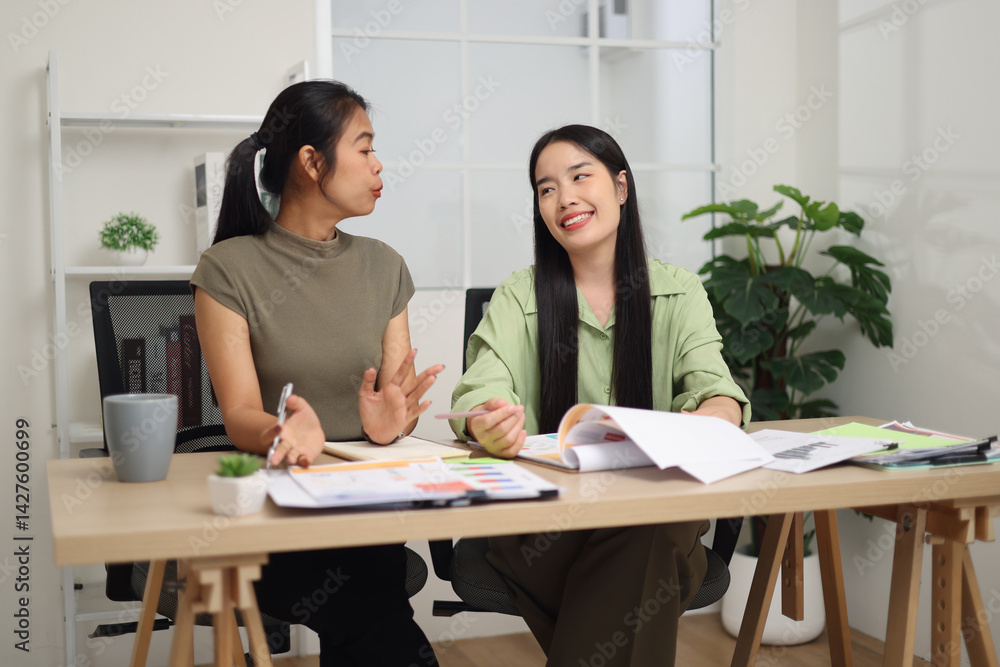 Portrait of Two female colleagues are sitting together at desk, reviewing documents and discussing work in the office.