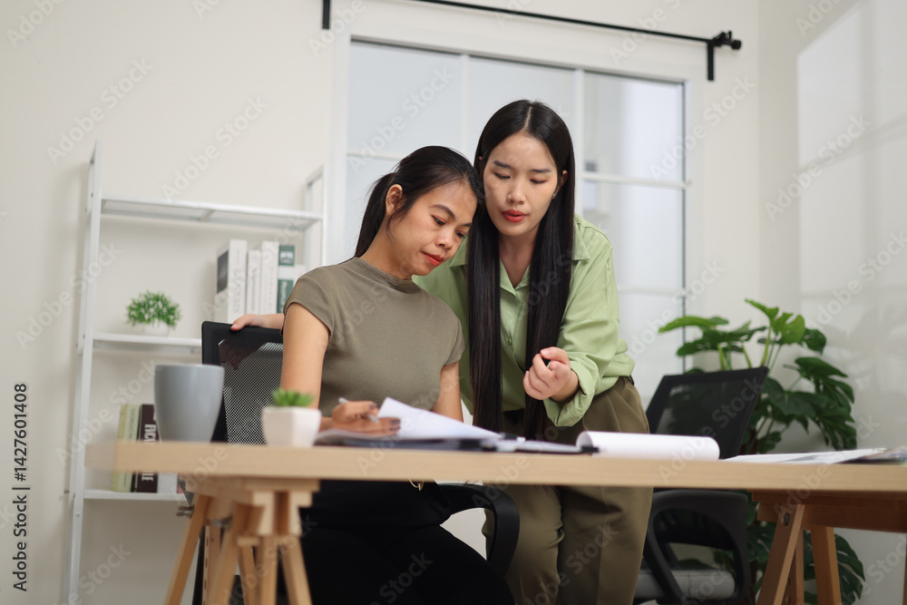 Low angle view shot, Two female colleagues are working together in an office. One stands explaining the work, while the other sits and listens with interest.