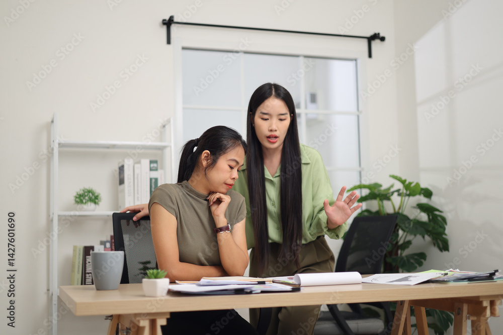 Portrait of Two female colleagues are working together in an office. One stands explaining the work, while the other sits and listens with interest.