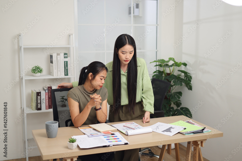 High angle view shot, Two female colleagues are working together in an office. One stands explaining the work, while the other sits and listens with interest.