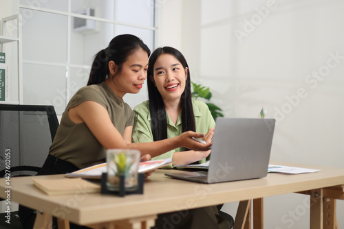 Portrait of Two Asian businesswoman are working together at a desk, discussing documents while looking at a laptop screen. Business ideas and strategies