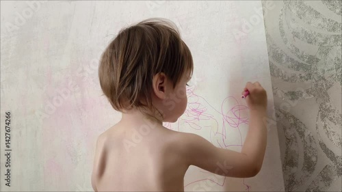 View from the back of child drawing with colored pencils the walls of his room. a child draws on the wall of a house