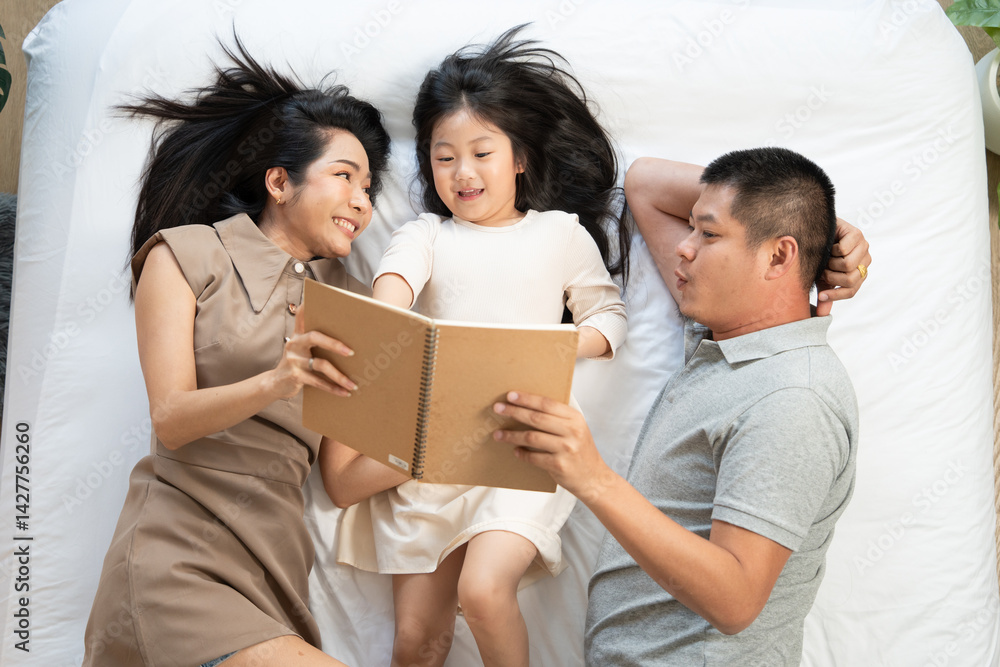 Obraz premium Top view of parent reading book with daughter on bed. happy family enjoy spending time together. Love bonding and insurance concept
