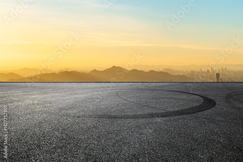 Asphalt road and mountain with city skyline at sunset