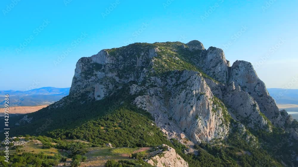A stunning panoramic view of a rugged, towering rock formation dominating the serene Tunisian landscape, surrounded by lush greenery and expansive plains under a clear blue sky. A stunning panoramic view of a rugged, towering rock formation dominating the serene Tunisian landscape, surrounded by lush greenery and expansive plains under a clear blue sky.