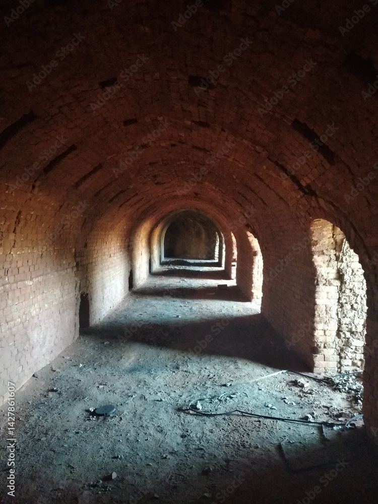 Obraz premium Tunnel interior with light at the end, photo of an old red brick arched tunnel with side passages flooded with sunlight.