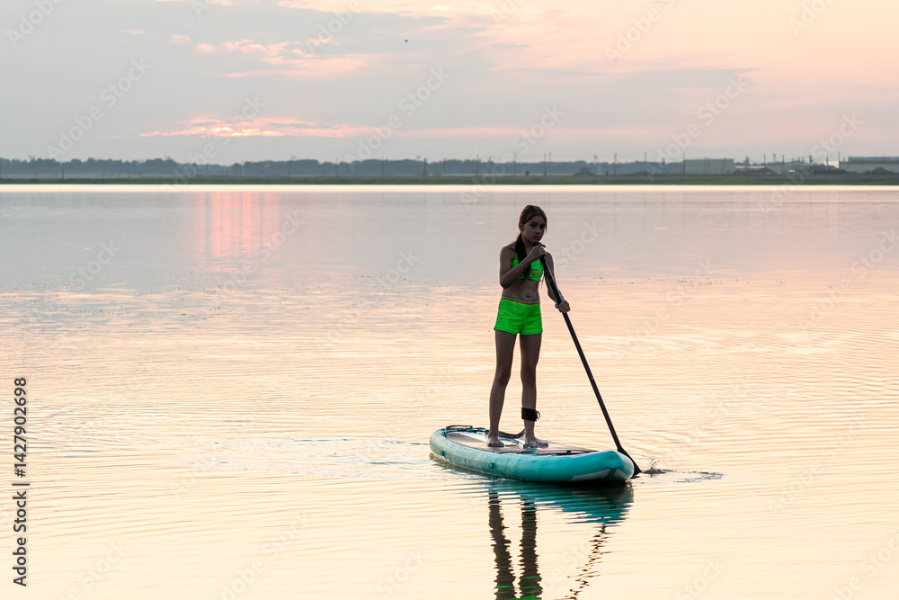 Girl paddling on SUP board on beautiful lake during sunset or sunrise standing up paddle boarding morning adventure in lake district