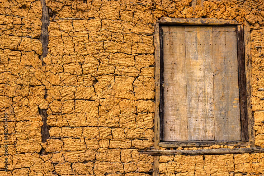 Detail of a traditional rammed earth wall with a rustic wooden window. The cracked texture reveals the beauty of this vernacular building technique.