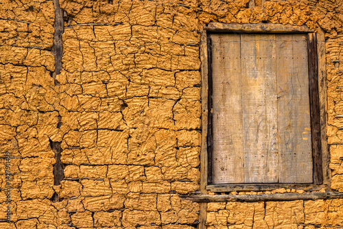 Obraz na płótnie Detail of a traditional rammed earth wall with a rustic wooden window. The cracked texture reveals the beauty of this vernacular building technique. w salonie