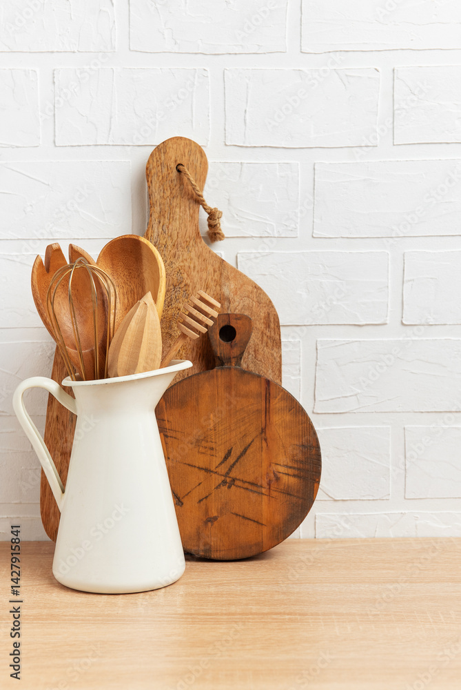 Kitchen utensils made of wood and metal resting on wooden table against white brick wall, concept of cozy home