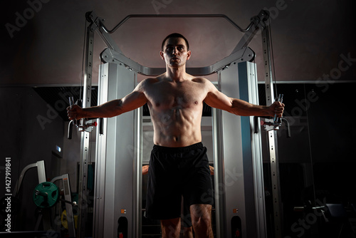 Obraz na płótnie Training young man in a dark gym at night on a simulator for pumping the muscles of the biceps and triceps. Rendezvous of hands along with heaviness. The athlete is swinging. w salonie