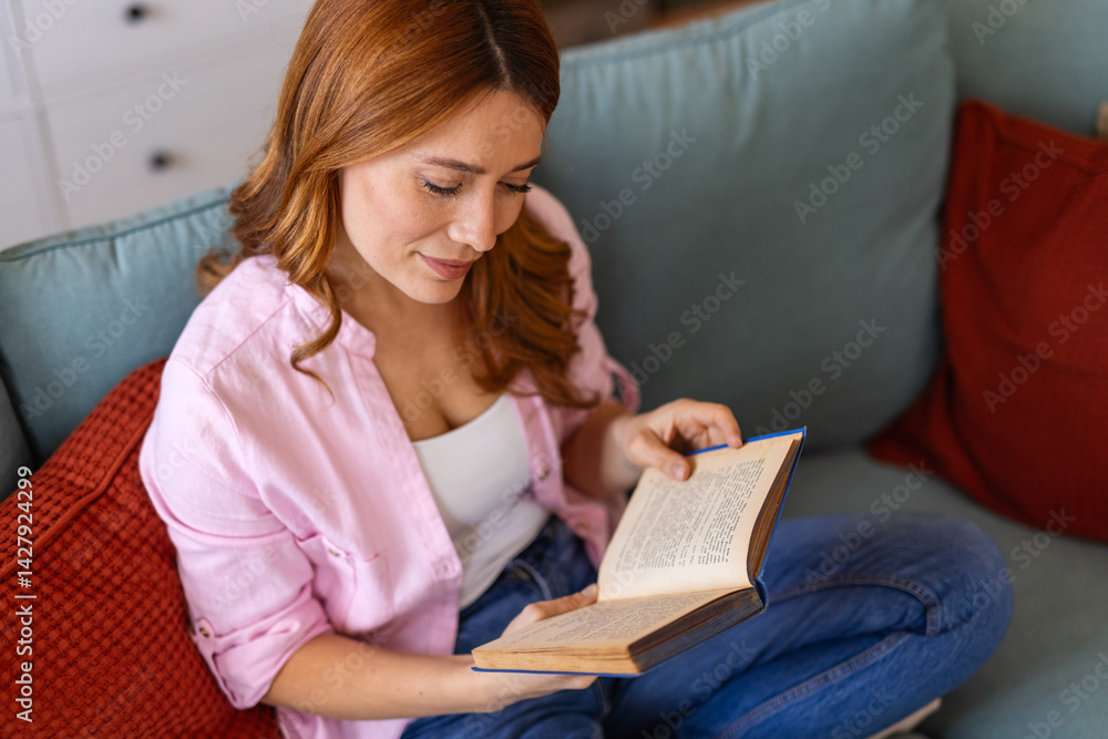 Woman is sitting comfortably on a sofa, absorbed in reading a book. She appears relaxed and focused, surrounded by a cozy home setting. The scene evokes a sense of tranquility and leisure Woman is sitting comfortably on a sofa, absorbed in reading a book. She appears relaxed and focused, surrounded by a cozy home setting. The scene evokes a sense of tranquility and leisure
