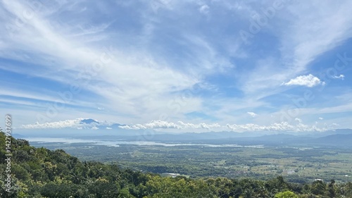 Stunning aerial view of a lush tropical valley in southern Wonogiri, Indonesia, with green fields, lakes, rural villages, and distant mountains under a bright blue sky. footage taken from Pokoh Hill.