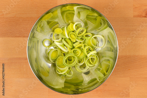 Obraz na płótnie A silver bowl contains a pile of sliced light green and white leeks on a light brown wooden surface w salonie