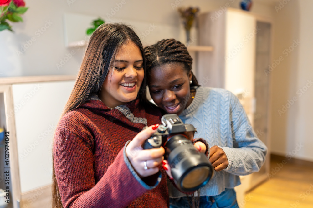 Two smiling female students reviewing photos on dslr camera at home