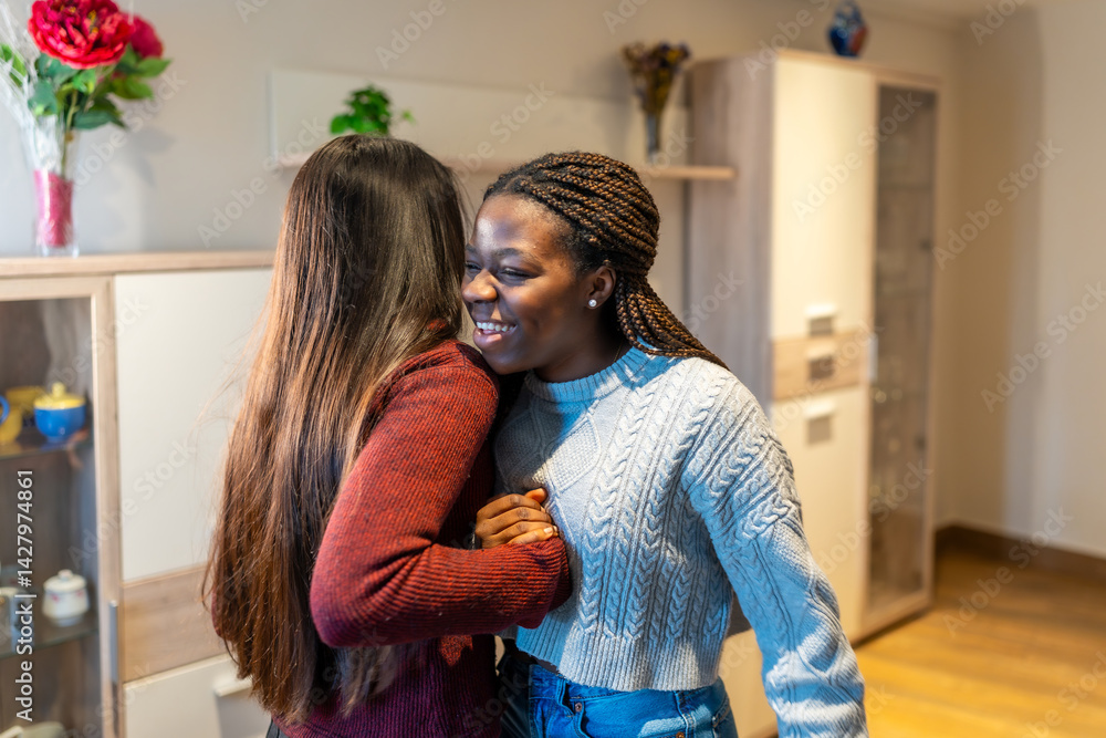 Two cheerful teenagers embracing and sharing secrets at home