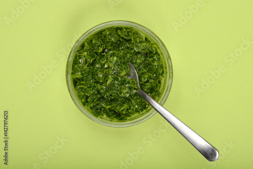 Obraz na płótnie A glass bowl of vibrant green wild garlic (Allium ursinum) pesto with a silver spoon is presented on a solid light green background from a top-down perspective w salonie