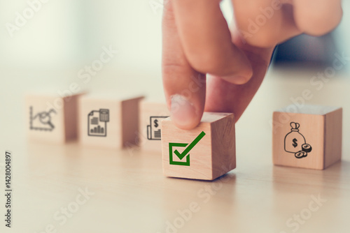 Financial approval concept. Wooden blocks with financial icons, hand  putting a green checkmark block, indicating successful authorization and completion of financial procedures.