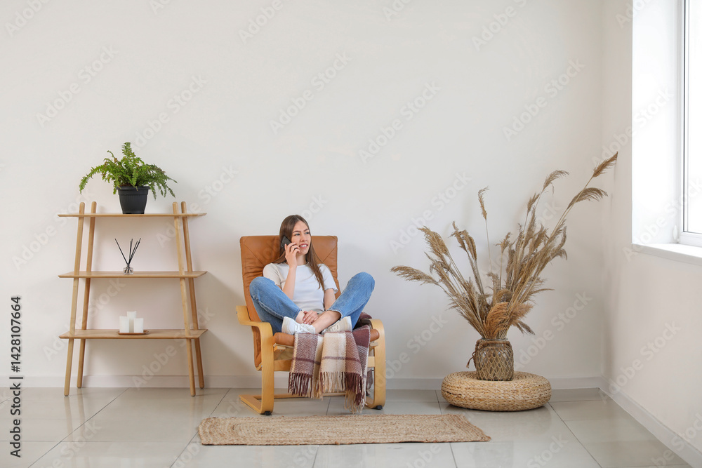 Young woman using mobile phone while sitting in armchair in room