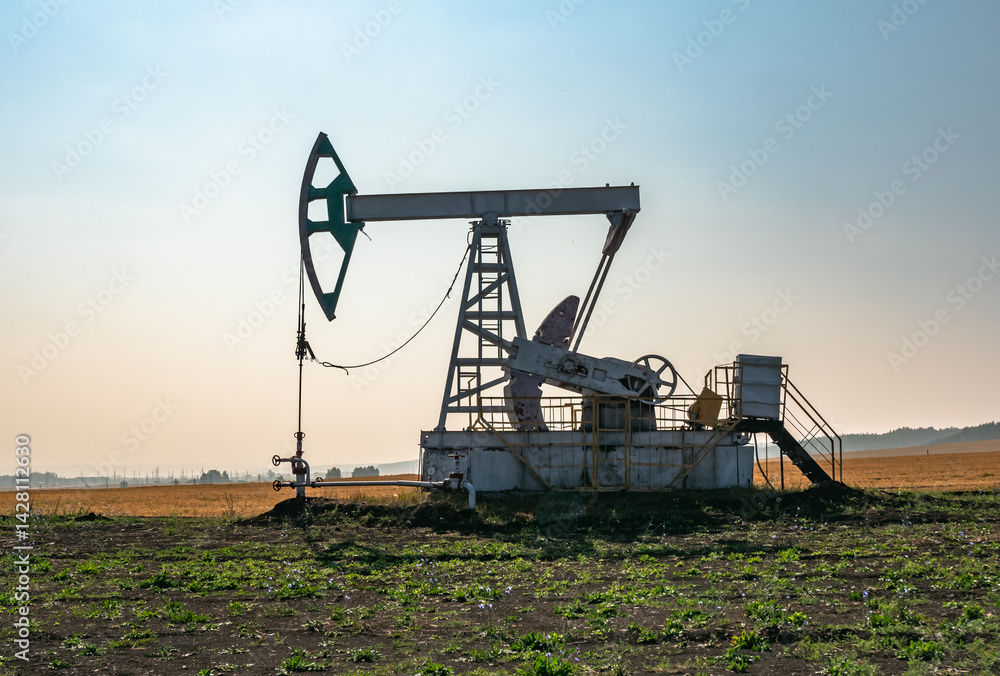 A large oil pump jack operates in an open field, extracting crude oil A large oil pump jack operates in an open field, extracting crude oil