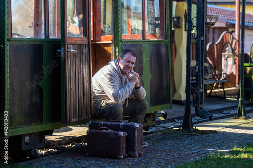 Obraz na płótnie Man sits outside vintage tram station with suitcase on a sunny day w salonie