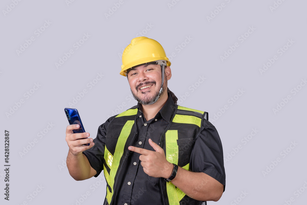 Smiling construction foreman in safety gear points at his phone, showing off a mobile app or receiving good news on site. Smiling construction foreman in safety gear points at his phone, showing off a mobile app or receiving good news on site.