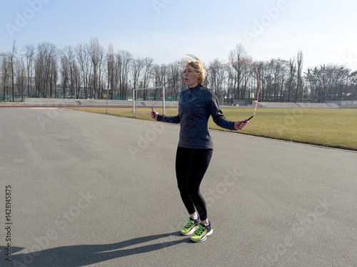  A girl in sportswear makes jumping rope outdoors (stadium), free space.