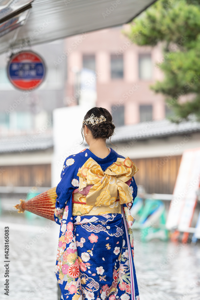 It's a rainy summer day. bus stop. A Japanese woman in a teenager wearing a blue kimono folding a Japanese umbrella.