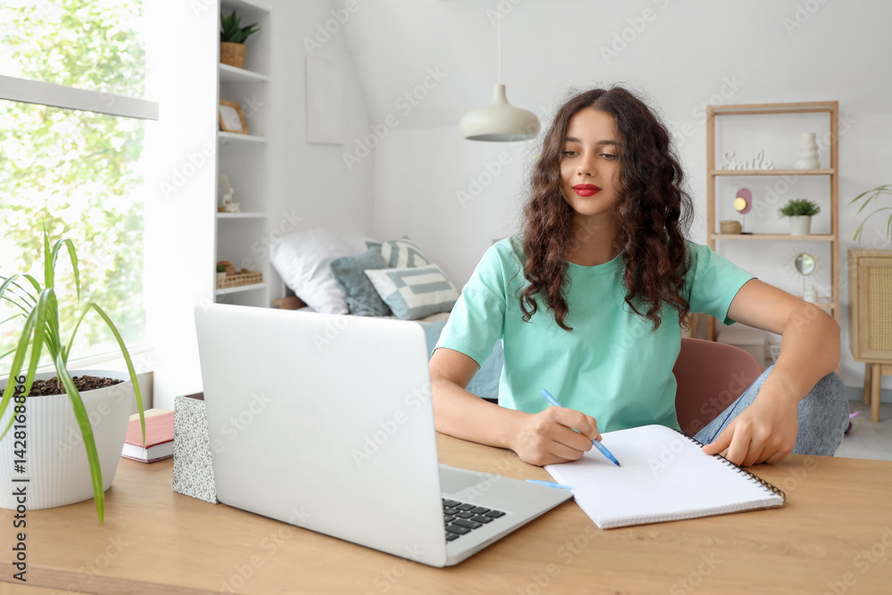 Teenage girl with notebook and laptop studying at table in bedroom Teenage girl with notebook and laptop studying at table in bedroom