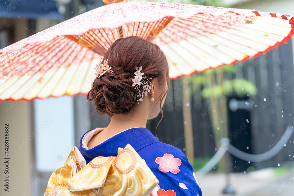 A local city in Japan on a rainy summer day. A Japanese woman wearing a blue teenage kimono holding a Japanese umbrella and climbing a slope. The back view.