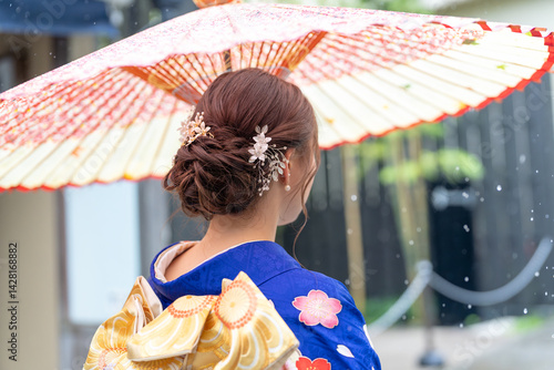Obraz na płótnie A local city in Japan on a rainy summer day. A Japanese woman wearing a blue teenage kimono holding a Japanese umbrella and climbing a slope. The back view. w salonie