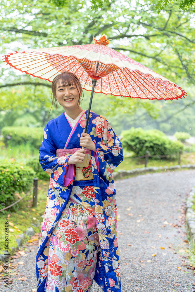 A local city in Japan on a rainy summer day. Japanese woman wearing a blue kimono for teenagers with a Japanese umbrella walking through a traditional garden.