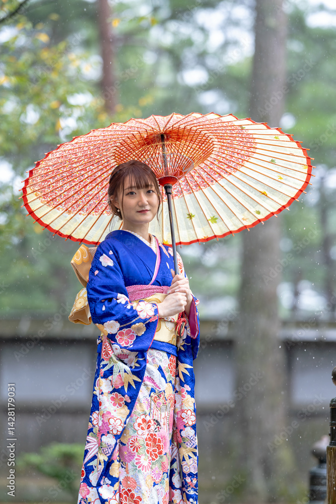 A local city in Japan on a rainy summer day. Japanese woman wearing a blue teenage kimono with a Japanese umbrella standing on a traditional garden bridge.