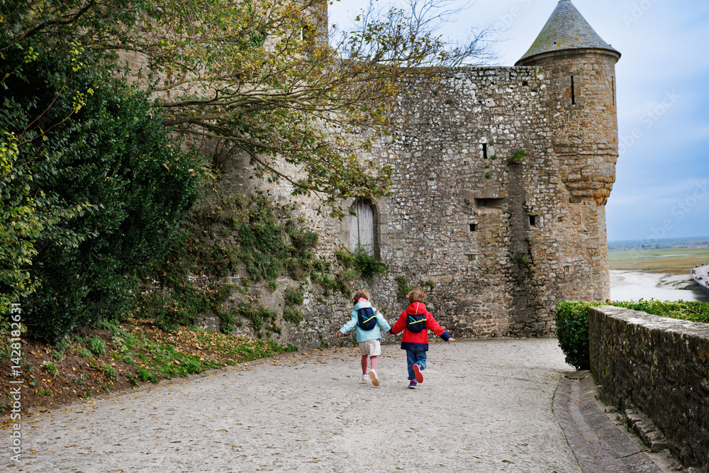 Kids in jackets run happily historic path of Mont Saint Michel