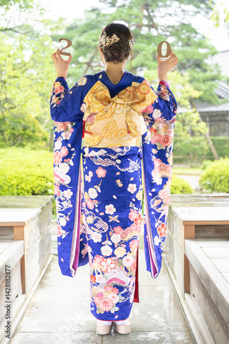 A local city in Japan on a rainy summer day. A Japanese woman wearing a blue teenage kimono in a traditional garden. She holds blocks of 2 and 0 in her hand. The back view.
