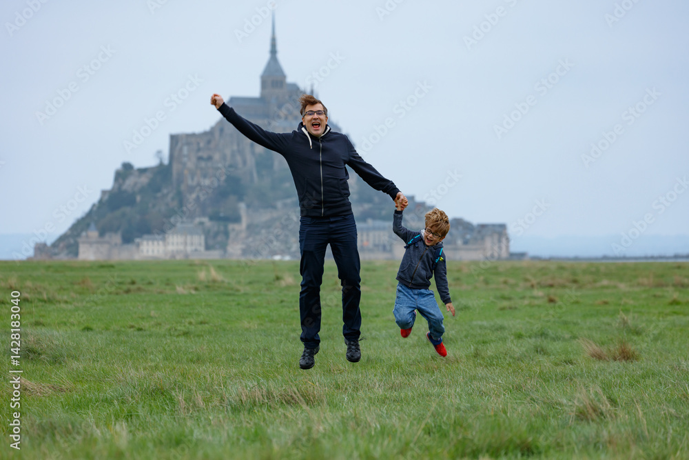 Father with son jumping near historic castle on a grassy field