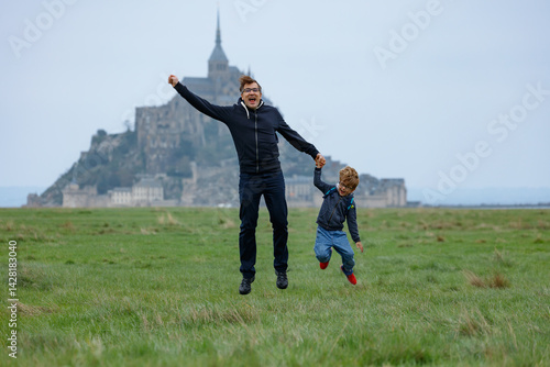 Obraz na płótnie Father with son jumping near historic castle on a grassy field w salonie