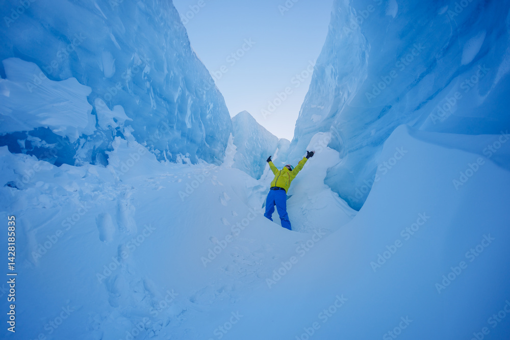 Explorer man celebrates in a deep snowy canyon with ice cliffs